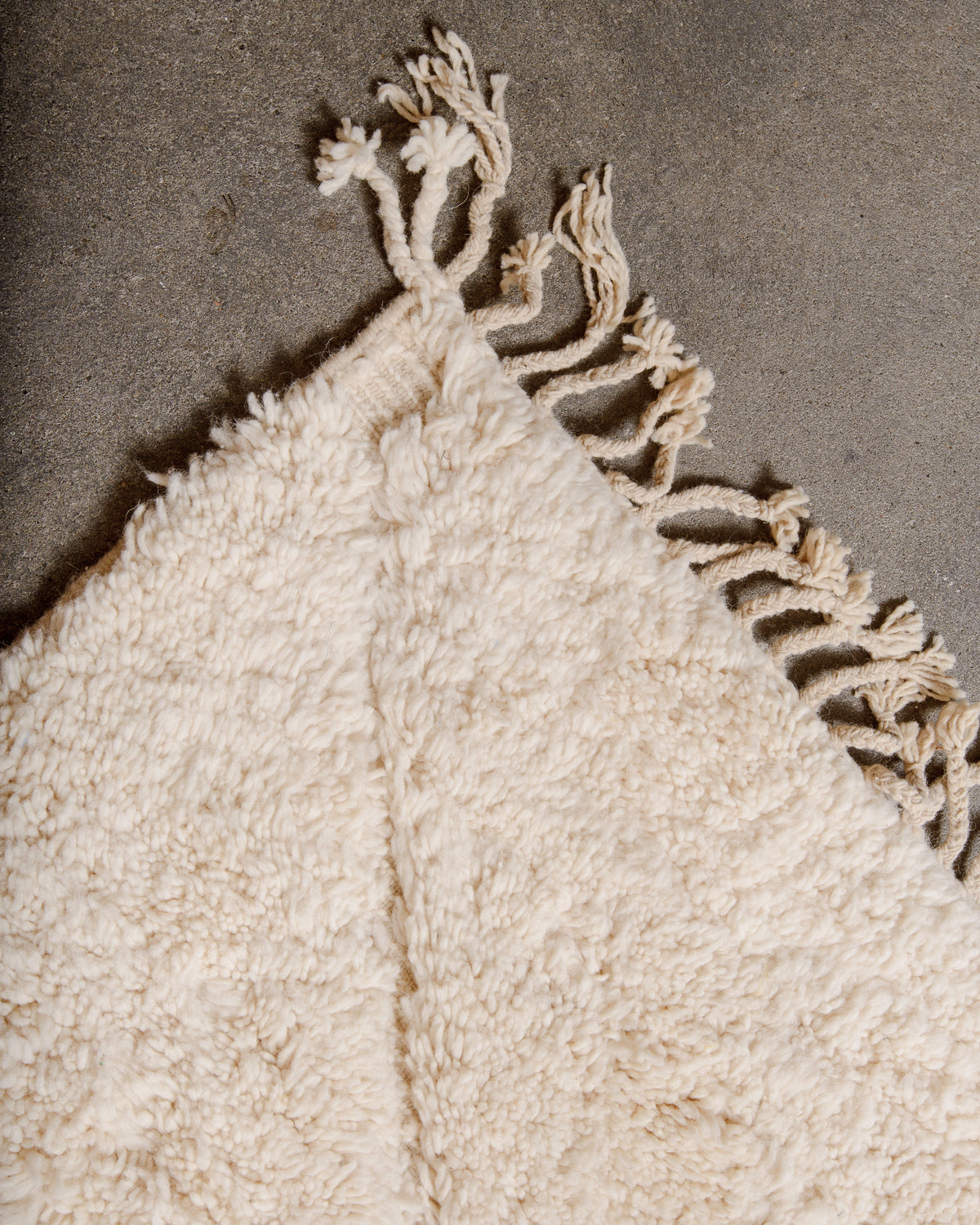 Corner of cream Beniourain rug with natural wool tassels.